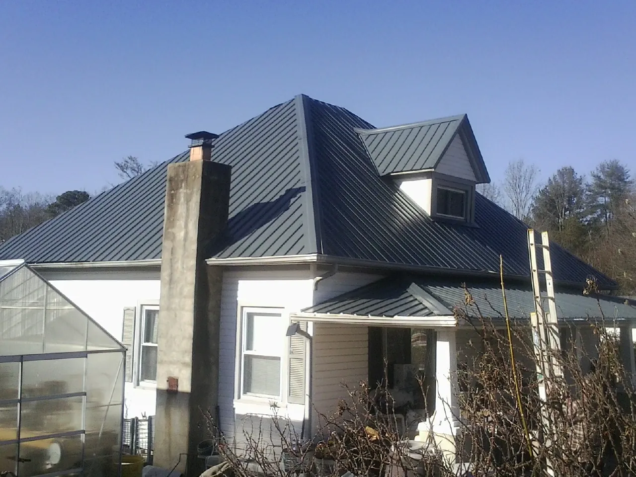 Dark blue standing seam metal roof on a white farmhouse with dormer — Slate & Tile Roof Repair by Roofing Brothers in Harveysburg