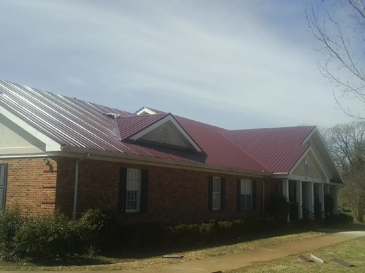 Red metal roof with gabled entries on a long brick building, from a Hail Damage Roof Repair job in Harveysburg