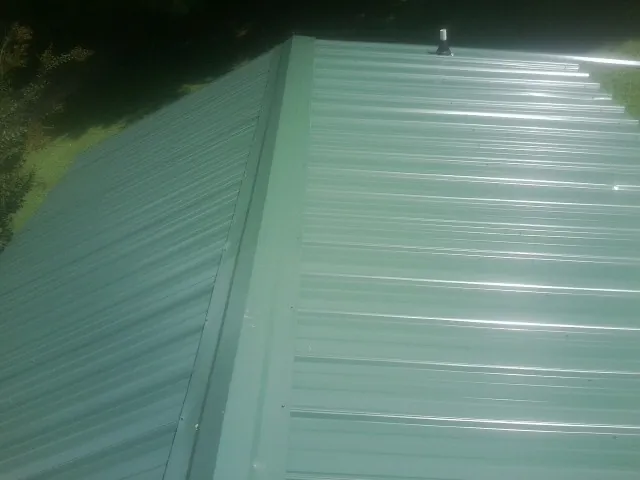 New green metal panels meeting at the ridge of a roof — Flat Roof Repair work by our crew in Harveysburg