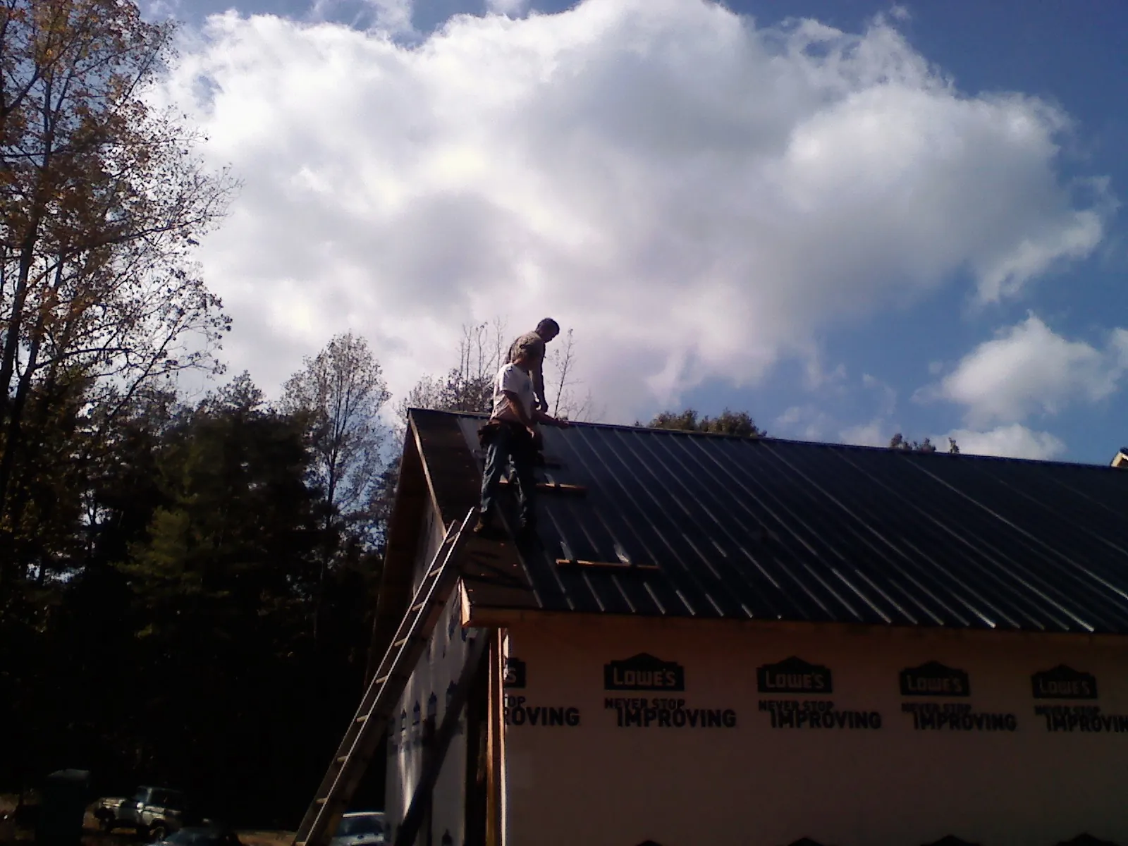 Roofer fastening dark metal panels high against a cloudy sky, from a Roof Inspection job in Harveysburg