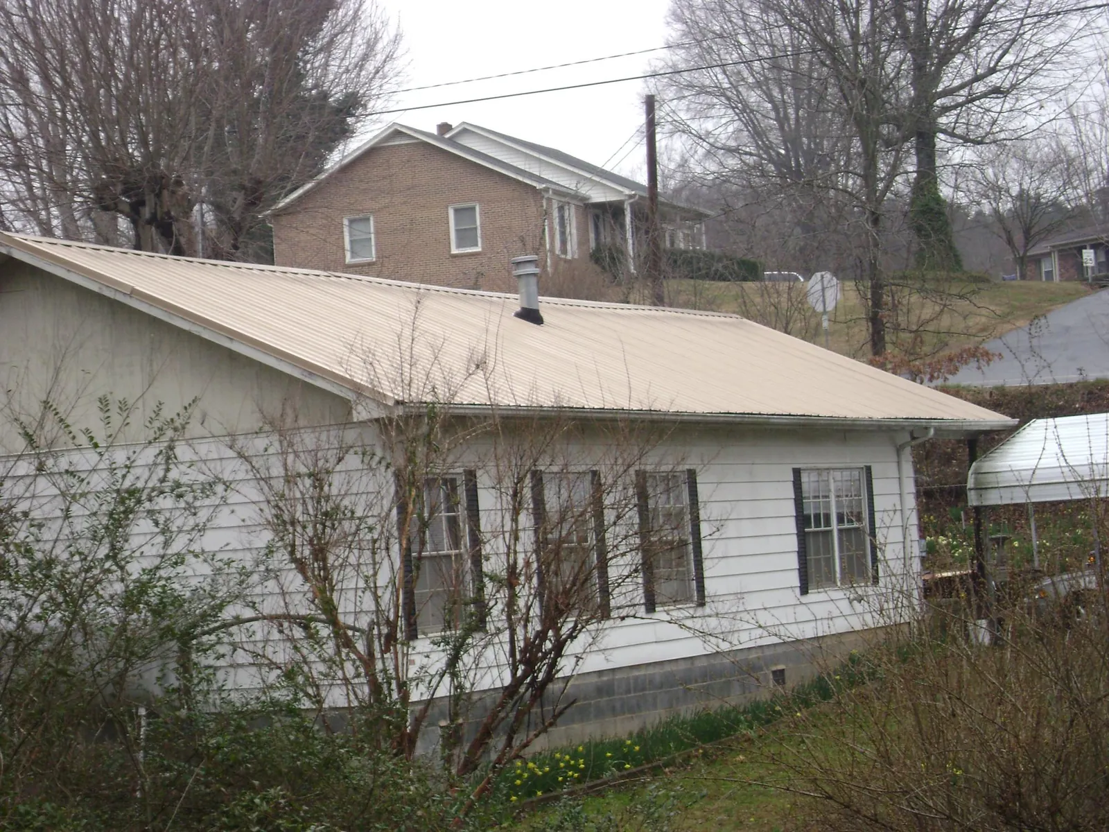 Tan metal roof on a white sided house set into a hillside — Commercial Roofing by Roofing Brothers in Harveysburg