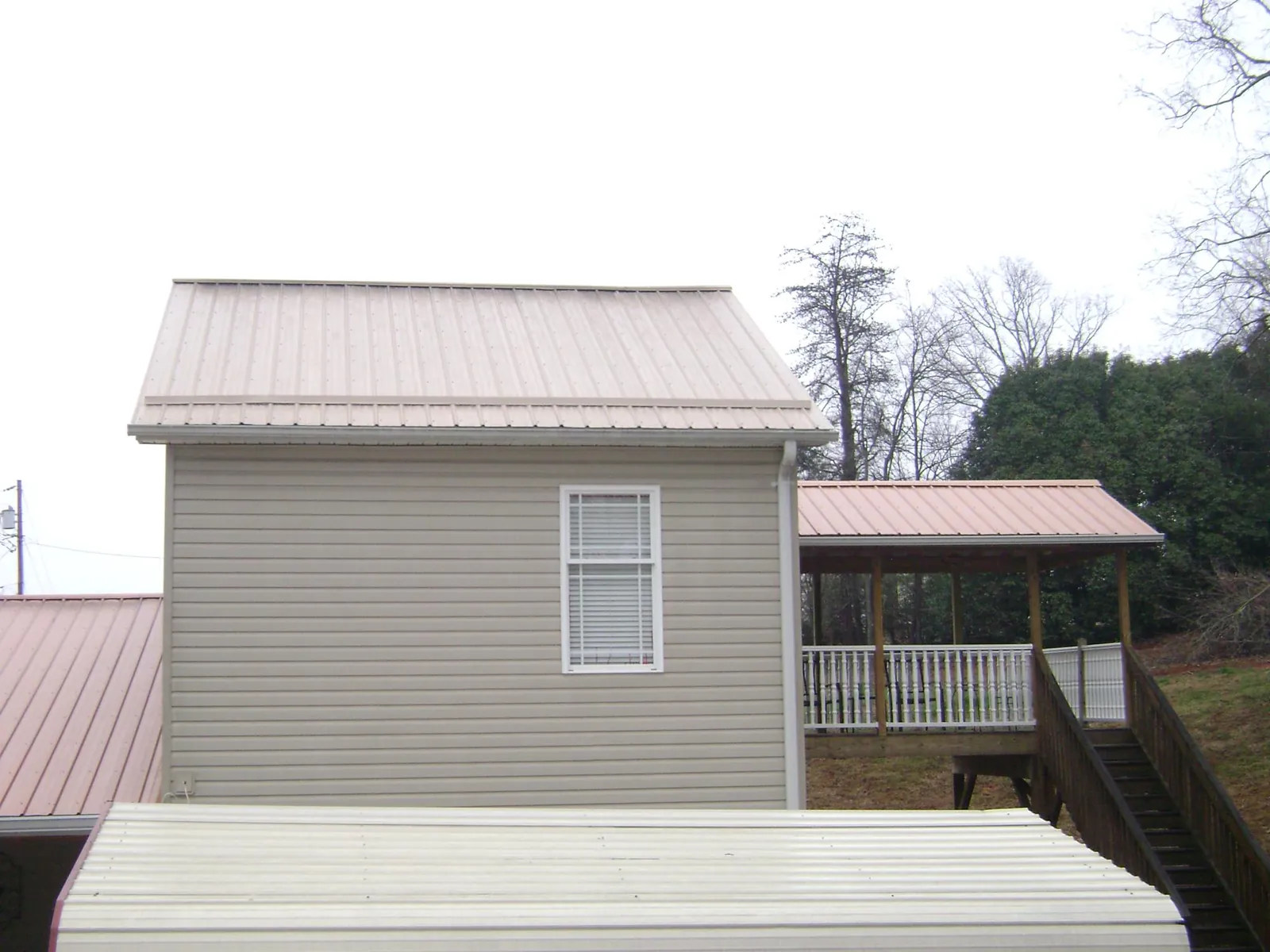 Tan metal roofs on a two story addition and attached porch, from a Roof Replacement job in Harveysburg